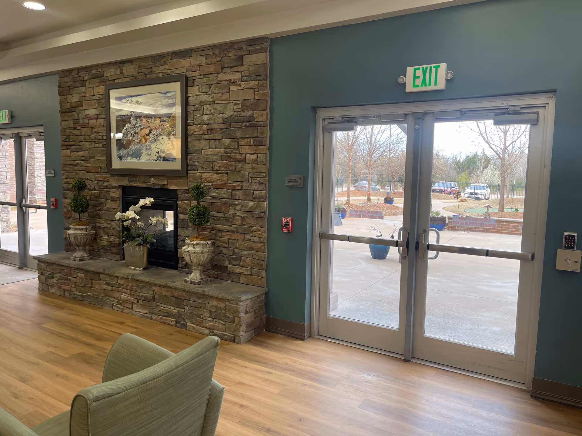 Lobby seating area with a stone fireplace, decorative plants and artwork, and double exit doors to the outside.