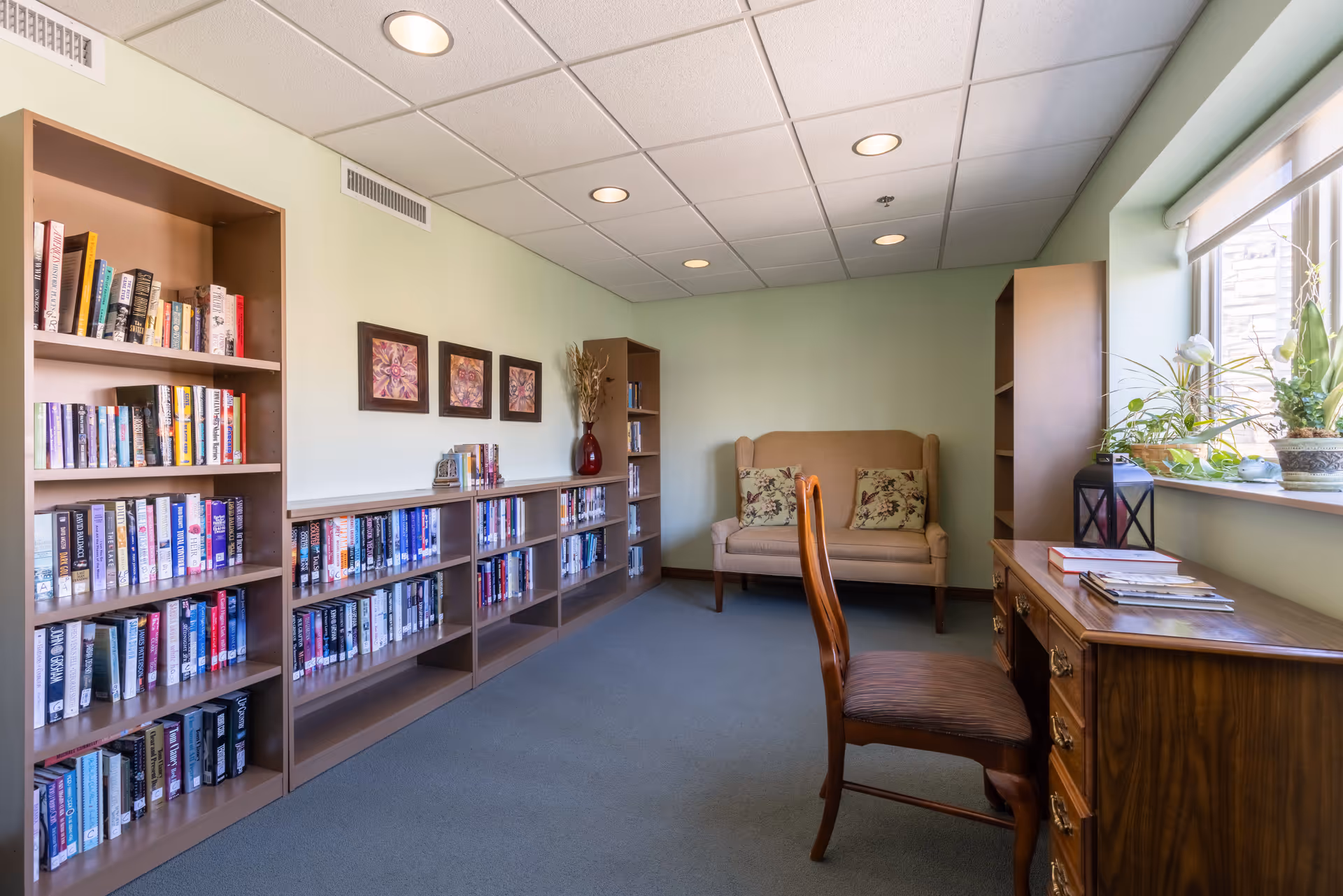 Small reading room with bookshelves, a desk and chair by a window, and a loveseat against a pale green wall.