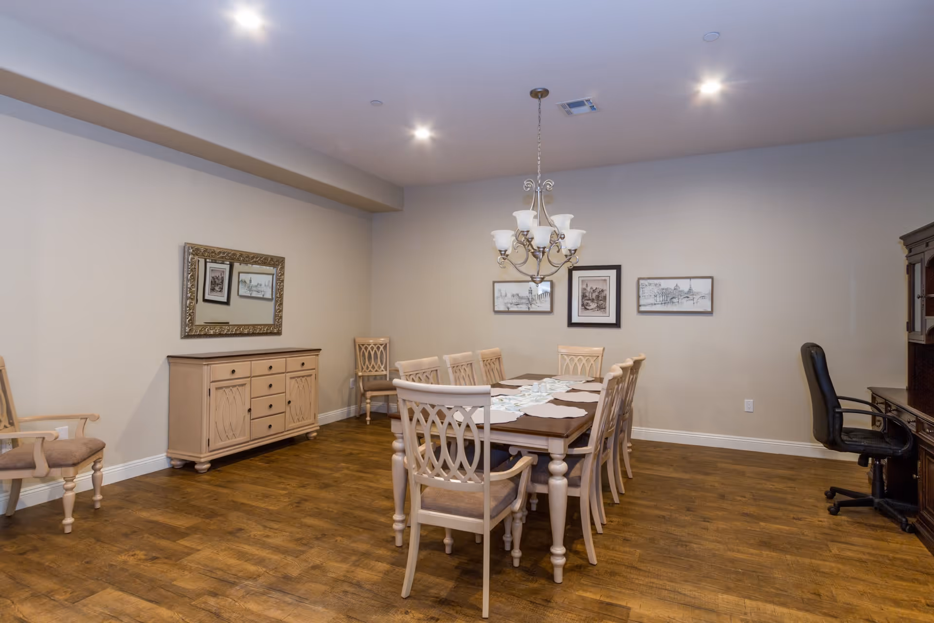A formal dining room with a long wooden table surrounded by chairs, a chandelier, sideboard, and framed artwork on the walls.