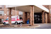 Entrance area of a senior living facility with a covered drop-off zone supported by brick pillars. An ambulance is parked under the covered area near the entrance doors.