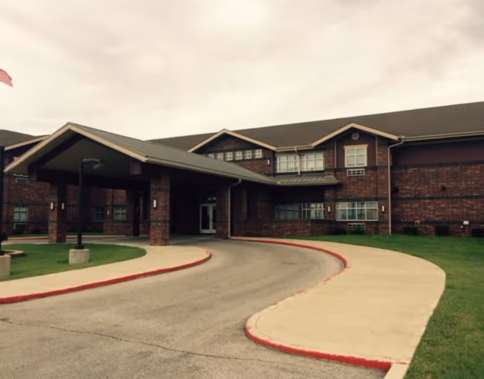 Front exterior view of Canoe Brook Assisted Living - Broken Arrow, showing a brick building with a covered entrance and a curved driveway bordered by a sidewalk and grass.