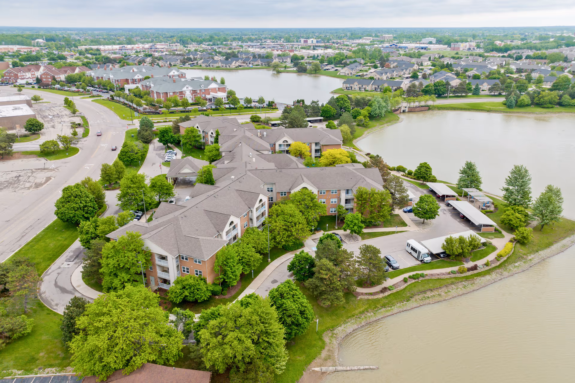 Aerial view of the Shorehaven senior living complex beside a lake, showing multiple connected brick buildings, trees, and driveways.
