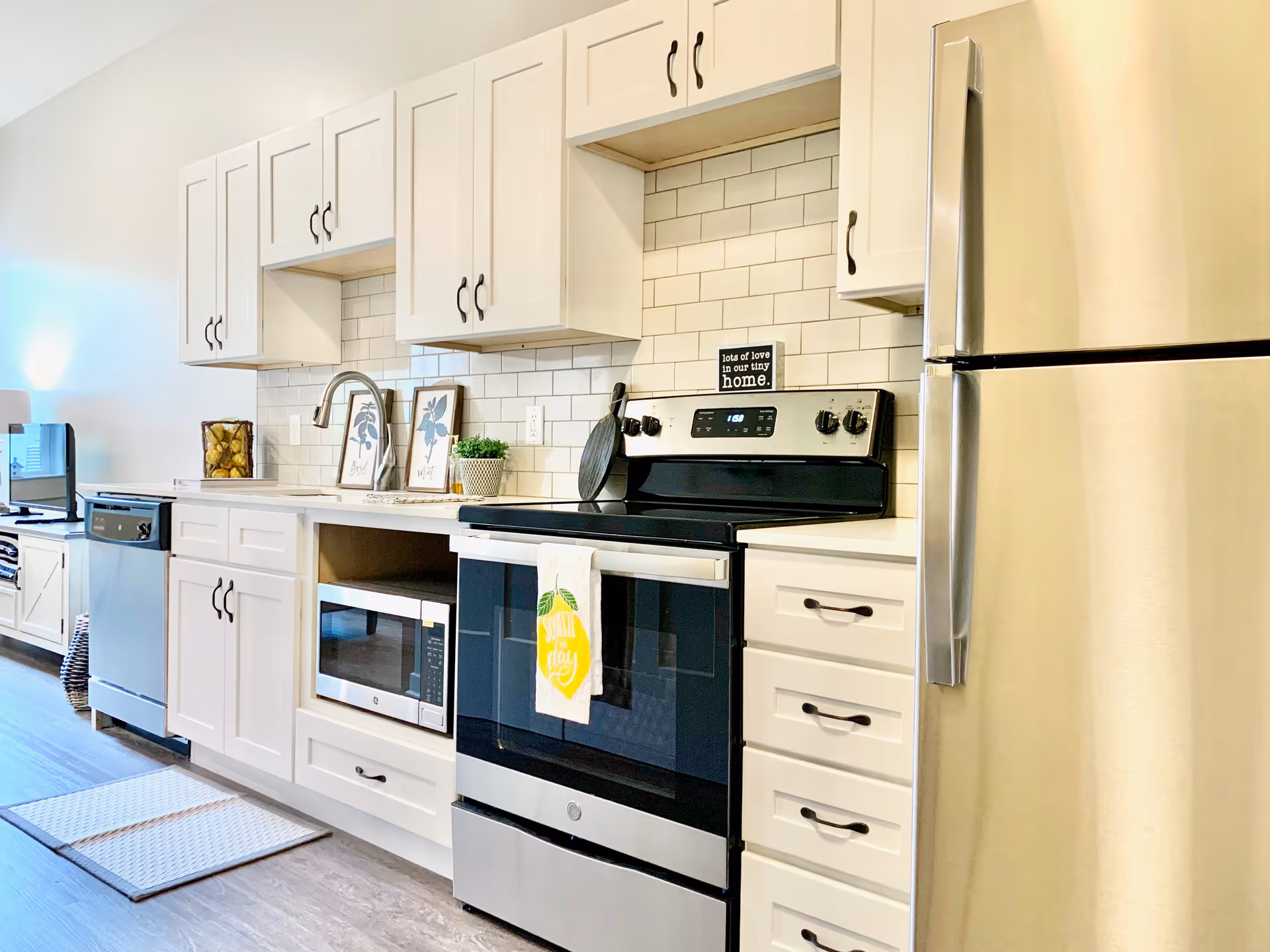 Bright modern kitchen with white cabinets, subway tile backsplash, stainless steel refrigerator and stove, microwave, and dishwasher.
