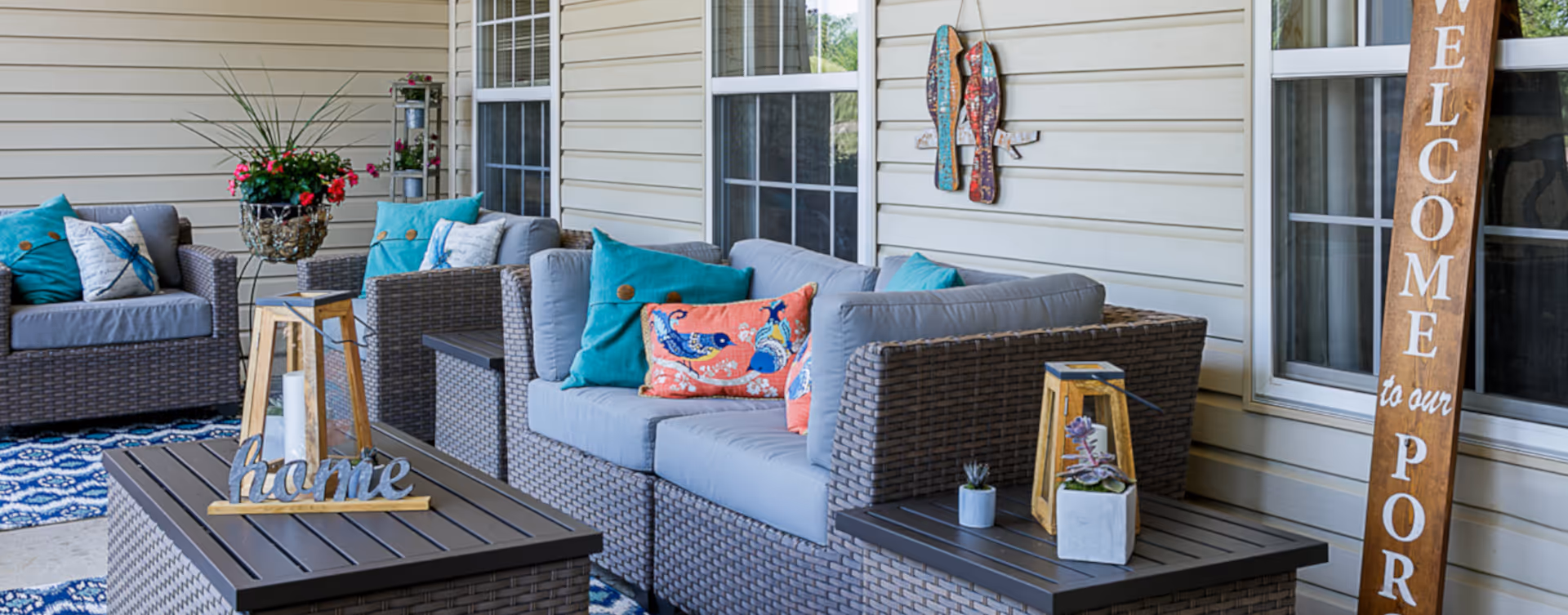 Covered porch with wicker patio sofas and colorful cushions arranged around a coffee table and decorative accents.