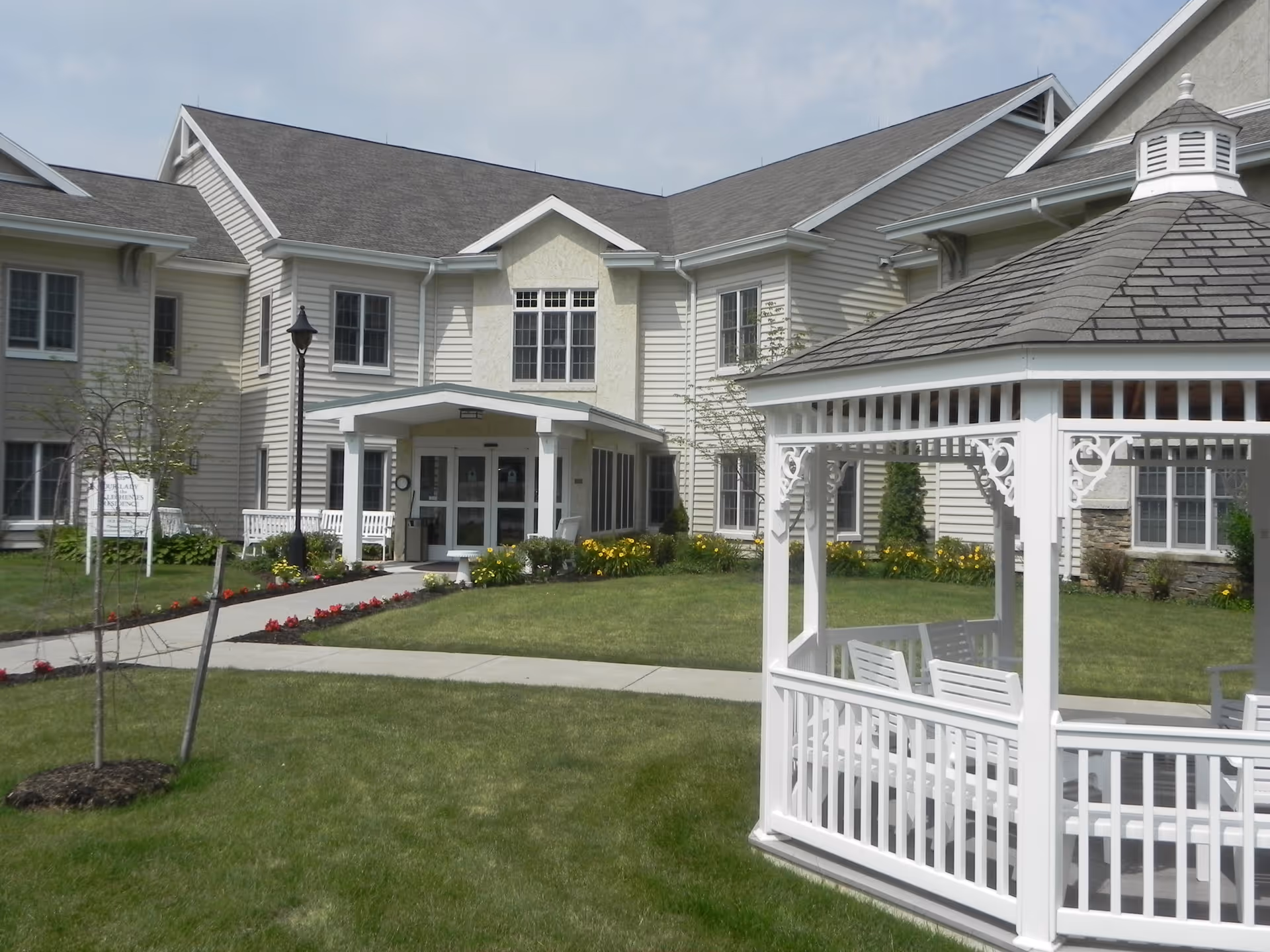 Front exterior of Garvey Manor Nursing Home showing a two-story building with an entrance porch and a white gazebo on the lawn.