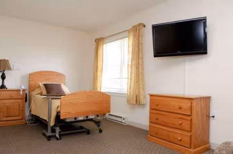 A furnished bedroom with an adjustable bed, wooden dresser, nightstand, and wall-mounted TV.