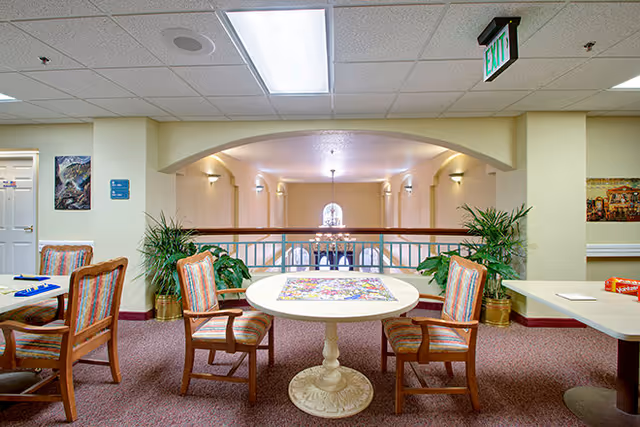 Bright senior living common area with a round table and four chairs overlooking a lower level through an arched opening.