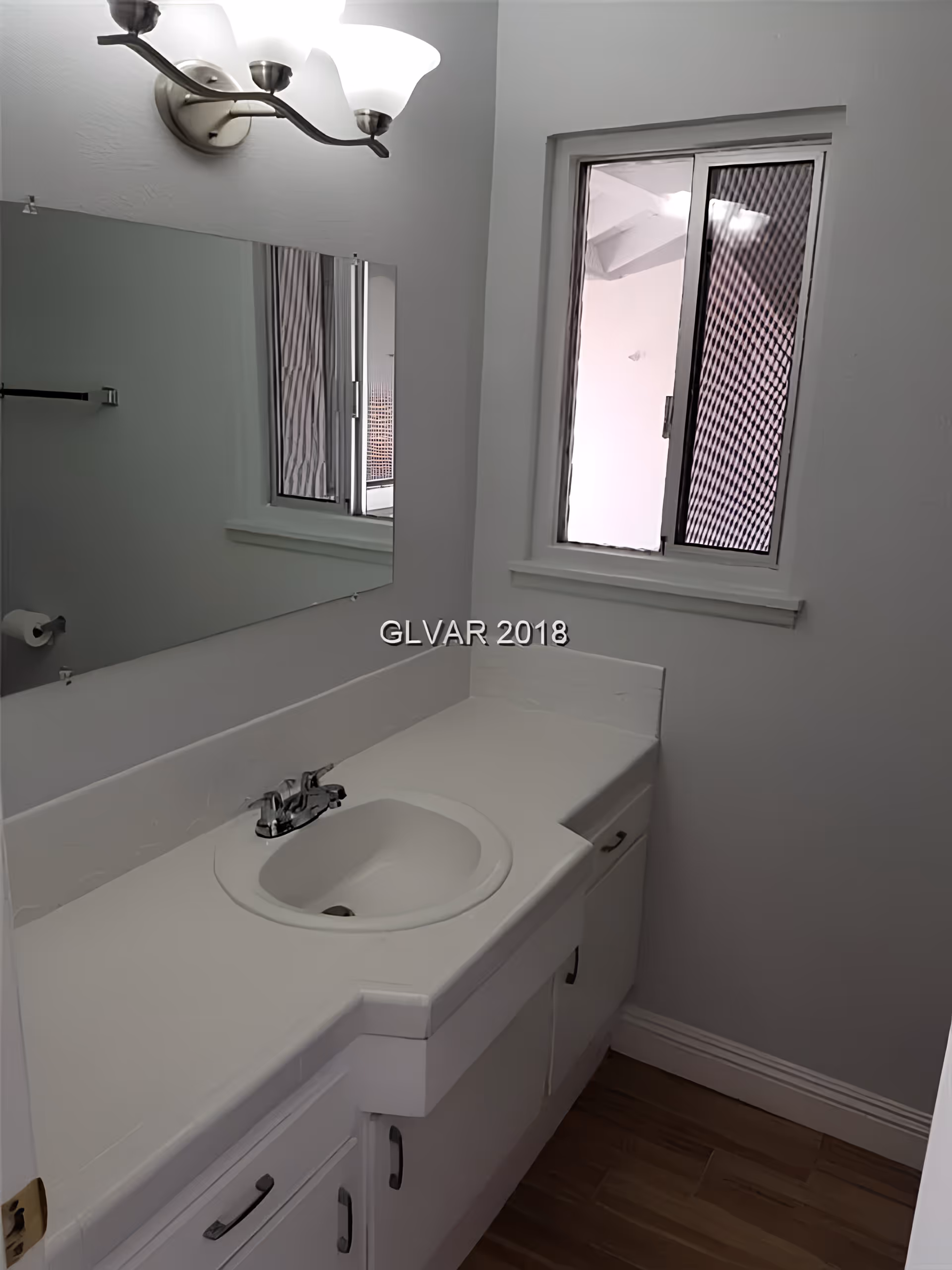 Small white bathroom vanity with sink, mirror, light fixture and a window.