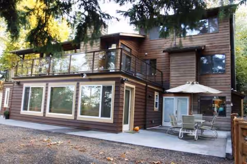 Two-story wood-clad senior living building with a patio, umbrella, and outdoor seating.