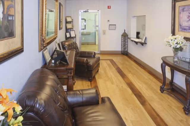 A furnished reception lounge with leather chairs, wood flooring, wall art, and a reception window.