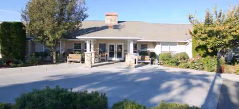 Single-story senior living facility front entrance with benches, landscaping, and a wide driveway.