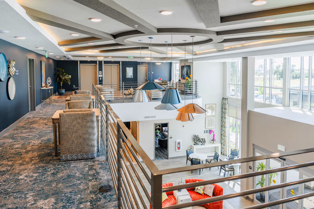 Bright two-story interior common area with a mezzanine walkway, pendant lights, and lounge seating below.