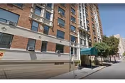 Brick multi-story residential building with a green awning over the main entrance along a city sidewalk.