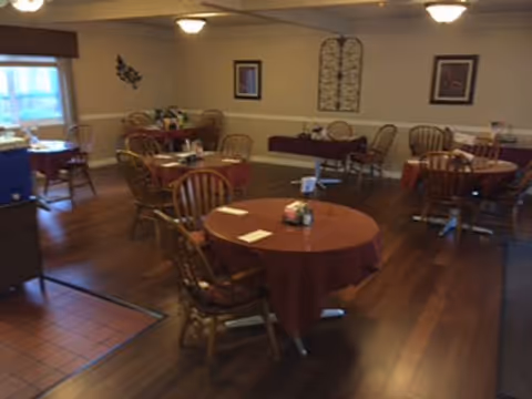 Dining room with round tables covered in burgundy tablecloths and wooden chairs on a hardwood floor.
