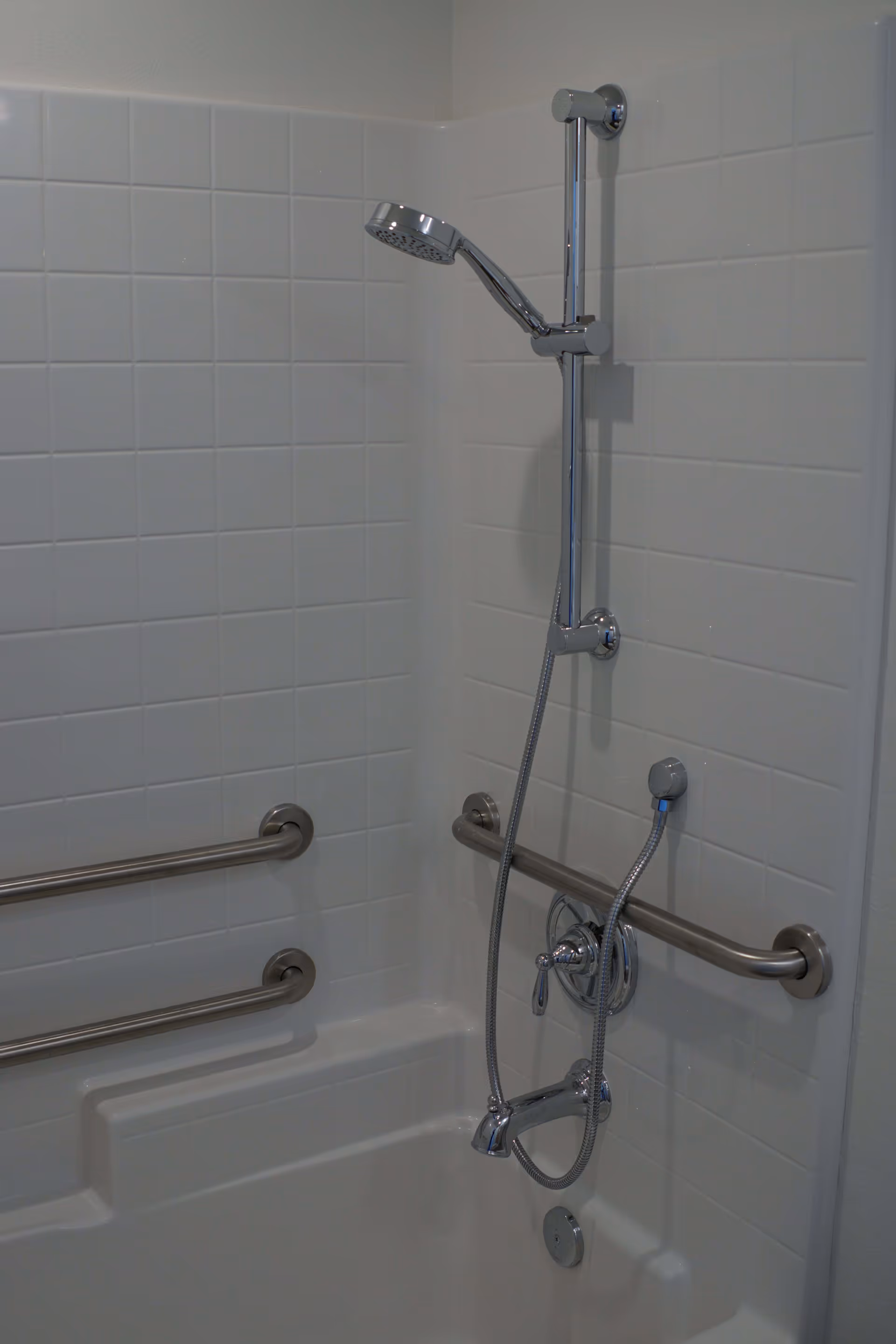 Tiled bathtub/shower corner with an adjustable handheld showerhead and stainless steel grab bars.