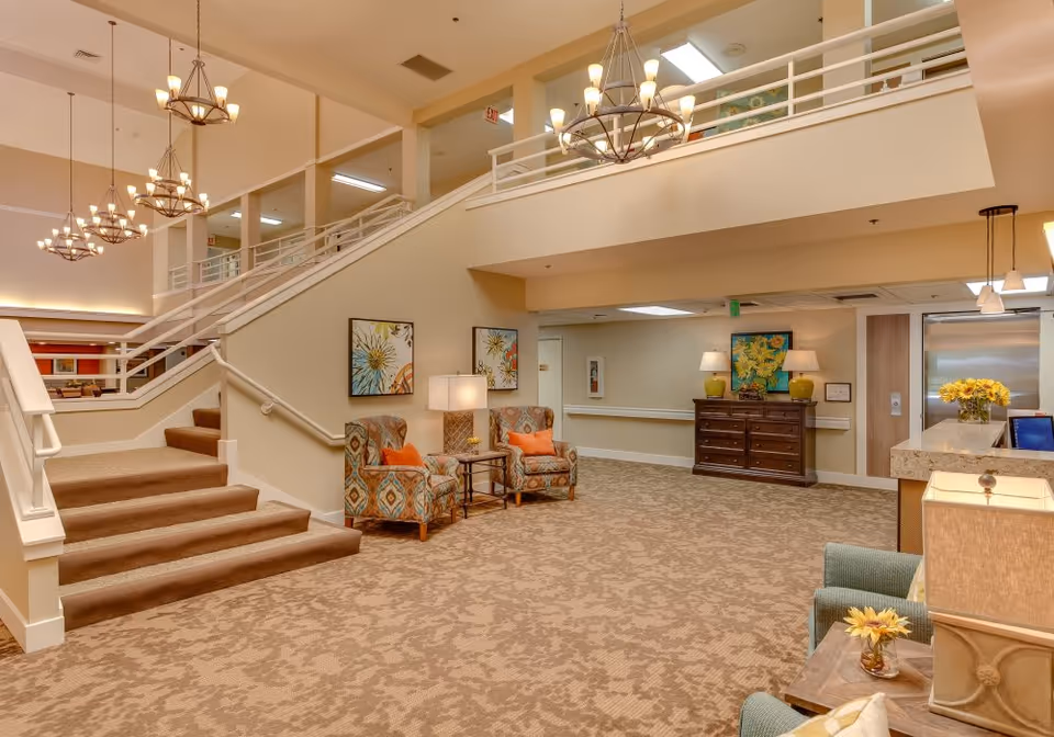 Spacious lobby with a carpeted staircase, upholstered chairs and tables, chandeliers, and a reception desk.