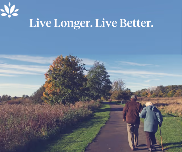 Two elderly people walking on a paved path through a grassy field with trees showing autumn colors under a blue sky. The text 'Live Longer. Live Better.' is displayed at the top on a blue background.