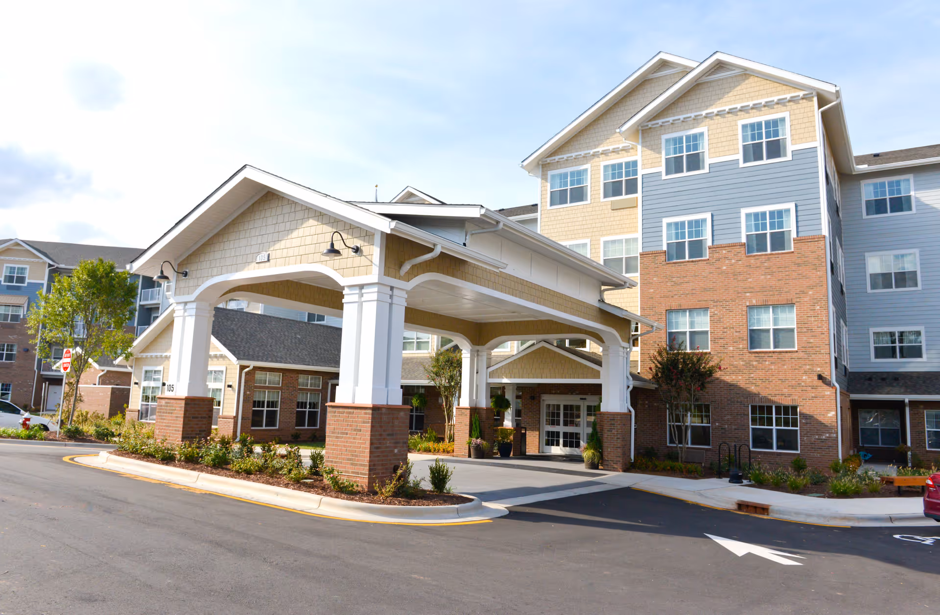 Front entrance of a multi-story senior living building with a covered porte-cochère and landscaped driveway.