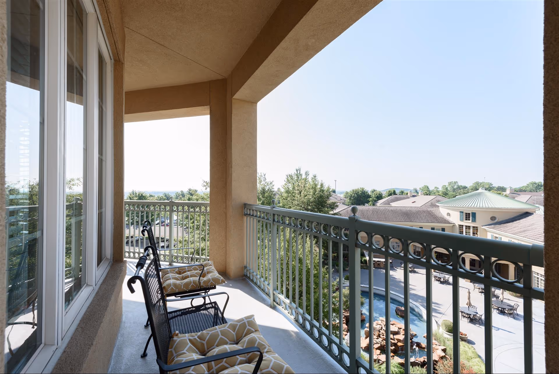 Covered balcony with cushioned chairs overlooking a courtyard and pool area.