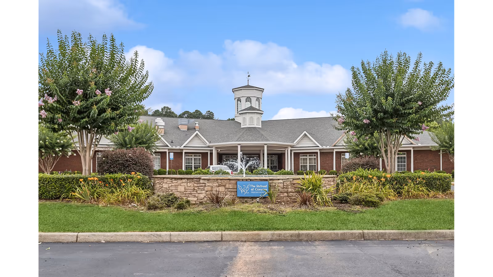 Front exterior of The Retreat at Conyers building with a landscaped lawn, fountain, and a sign in the foreground.