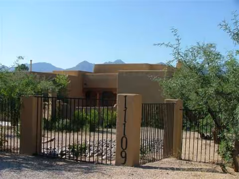 Front exterior of a desert-style senior home with a metal gate and stone pillars.