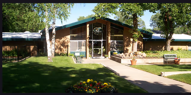 Front view of Aspen Assisted Living entrance with green lawn, trees, and walkway.