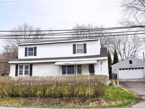 Front view of a white two-story house with black shutters and a detached garage.