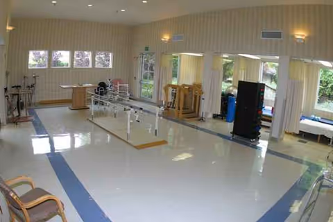 Interior of a senior care rehab gym with parallel bars and therapy equipment.
