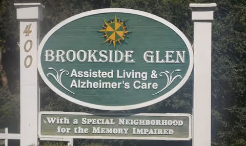 Outdoor sign for Brookside Glen Assisted Living & Alzheimer's Care with the address number 400 on the left post. The sign also states 'With a Special Neighborhood for the Memory Impaired' and features a sun emblem at the top.