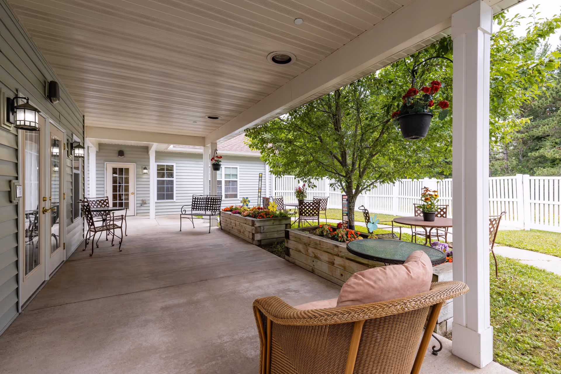 Covered outdoor patio with chairs, tables, raised flower planters, and a fenced grassy yard.