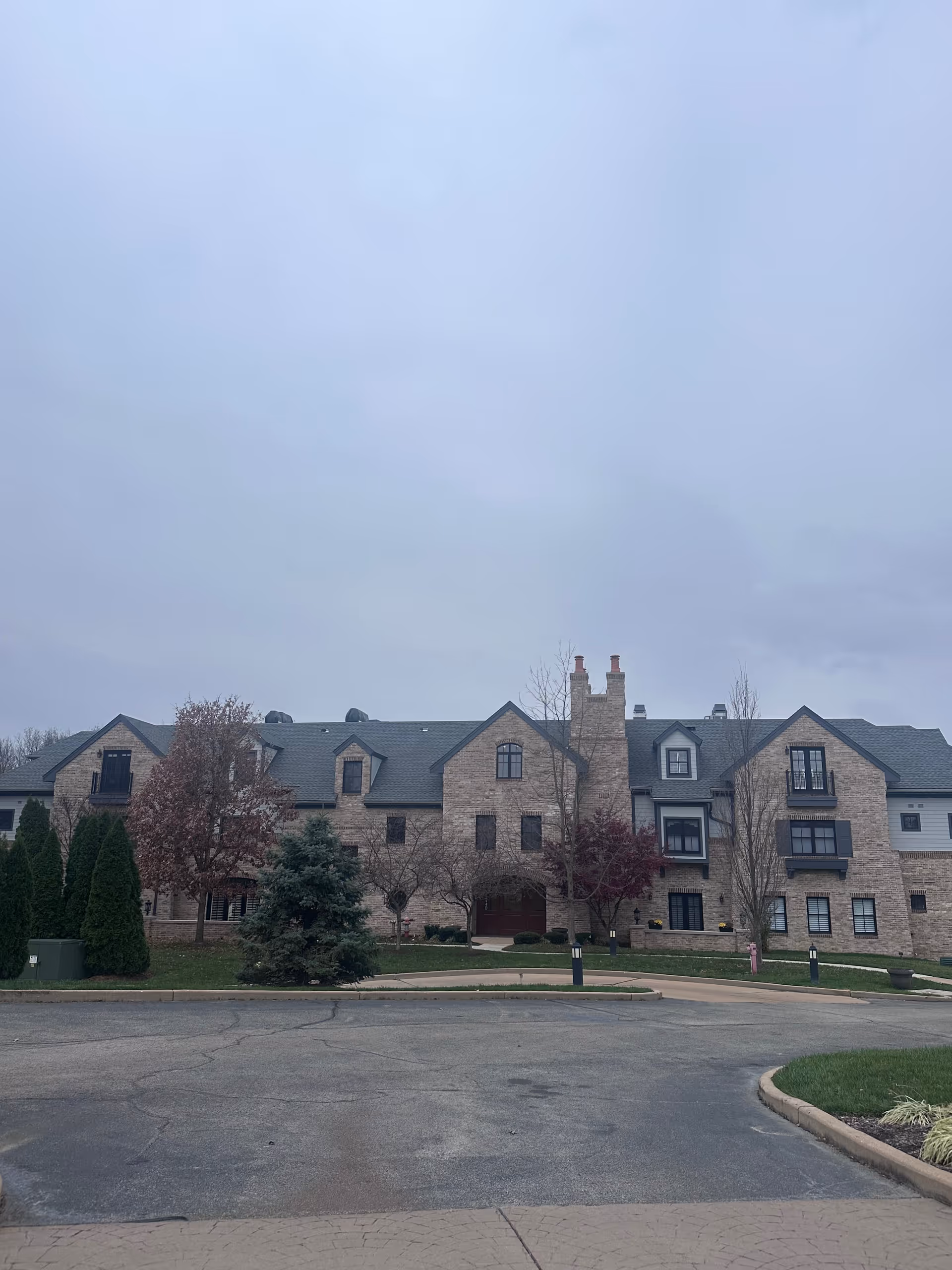 Stone-faced multi-story senior living building with a pitched roof and trees in front under an overcast sky.