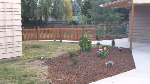 Exterior view of Affable Caring facility showing mulch beds, small shrubs, and a wooden fence.