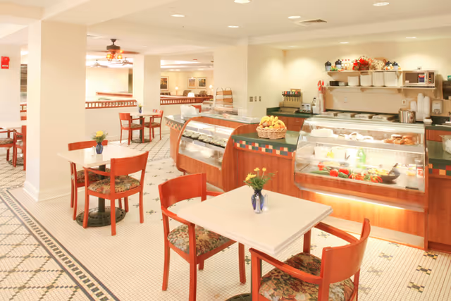 Bright dining area with small tables and chairs and glass food display cases at a service counter.