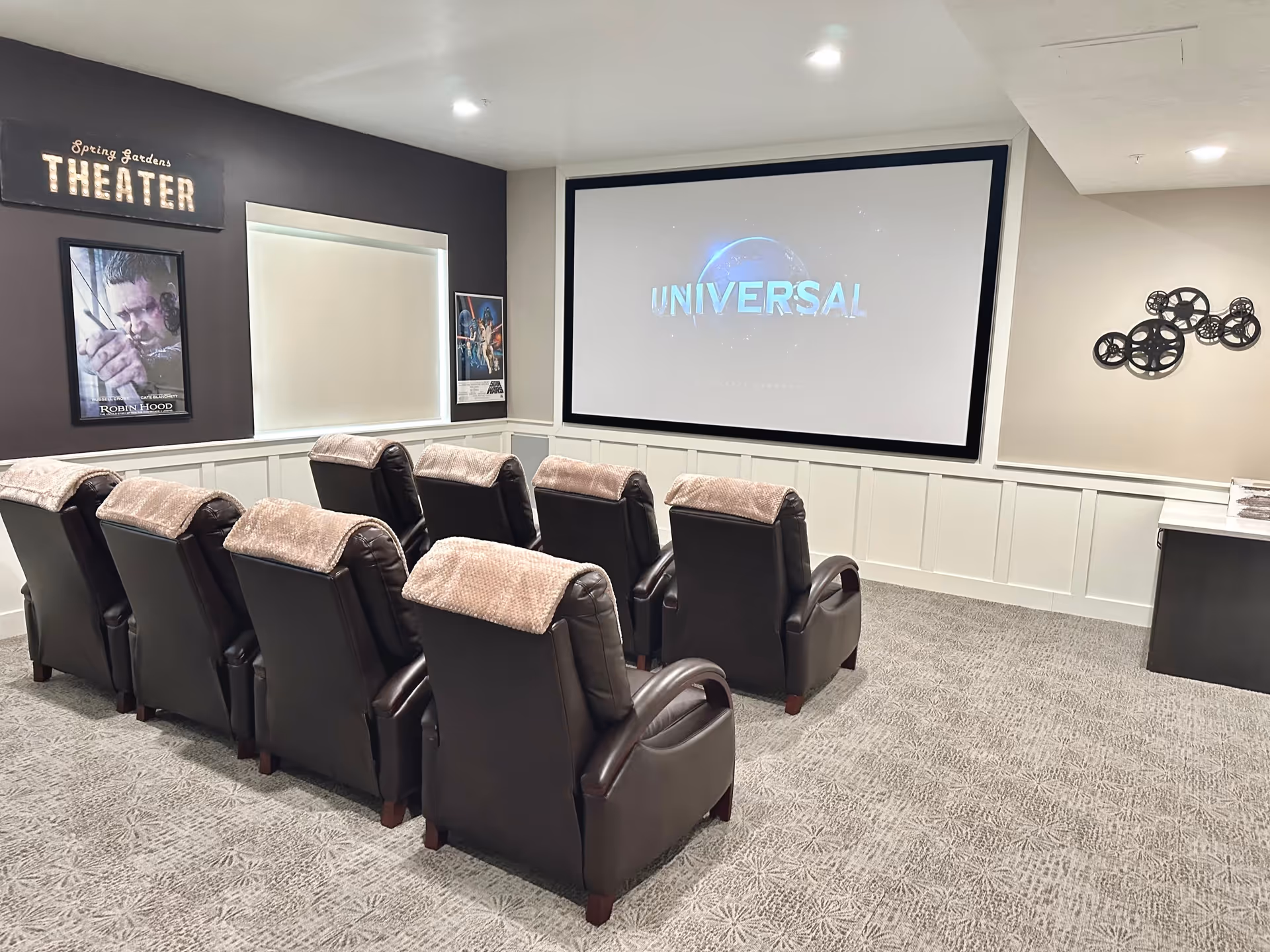 Small screening room with two rows of leather recliners facing a large projection screen displaying the Universal logo.