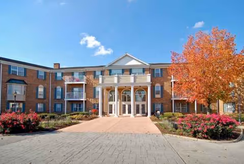 Brick senior living building with glass doors and autumn landscaping at the entrance.