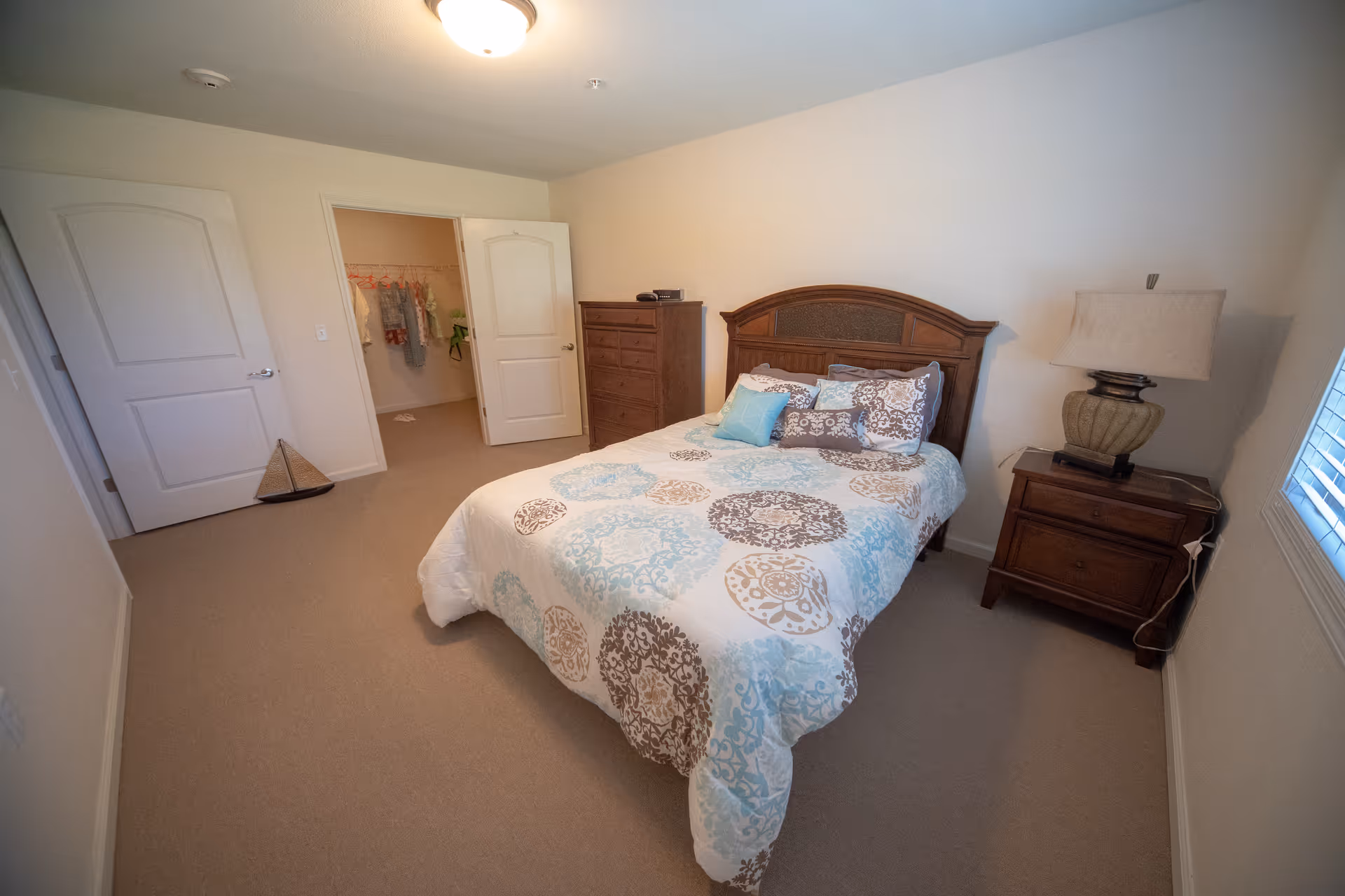 Spacious bedroom with a bed dressed in patterned linens, wooden headboard, nightstand, dresser and an open closet.