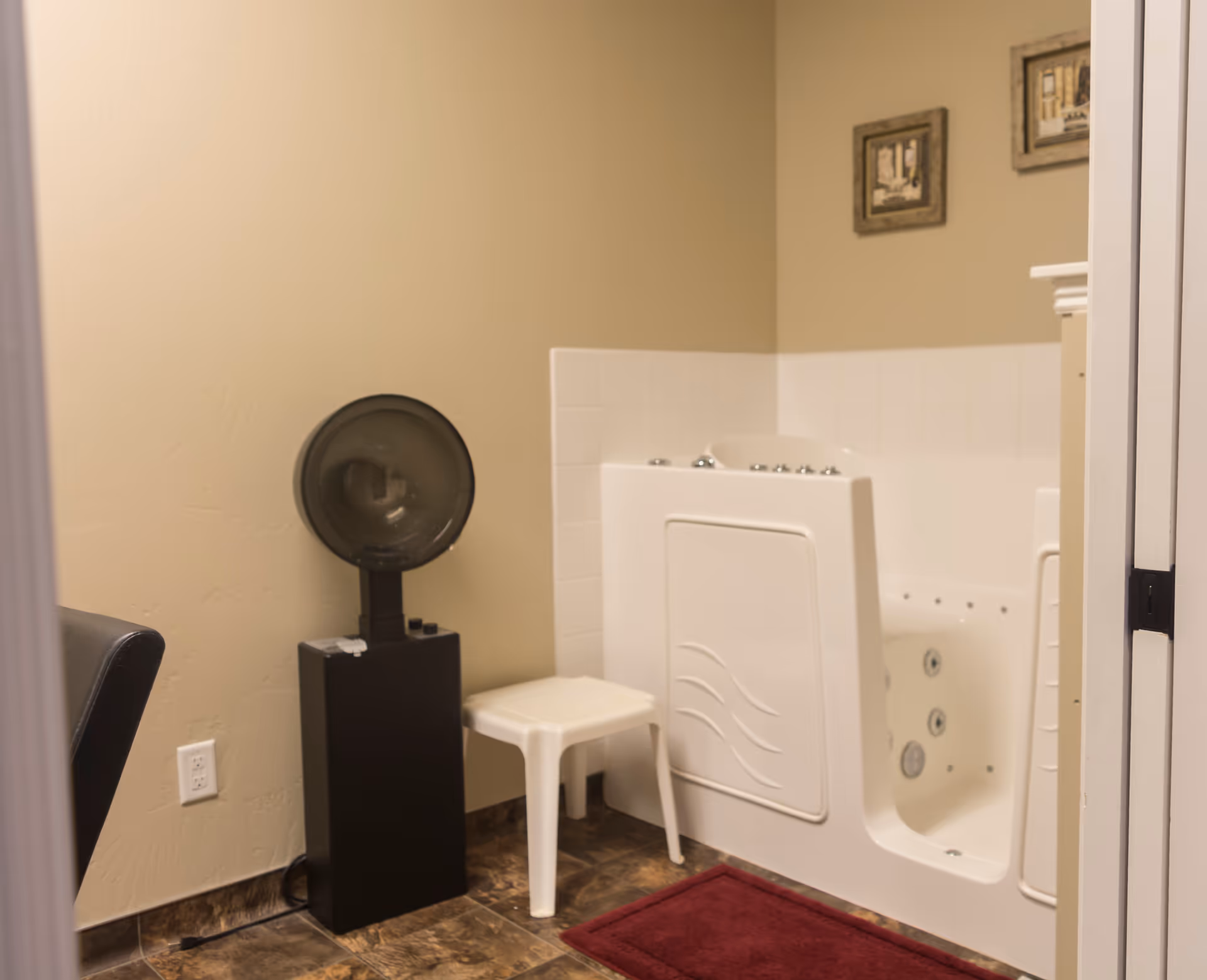 Walk-in bathtub with a small plastic stool and a hooded salon dryer in a beige bathroom.