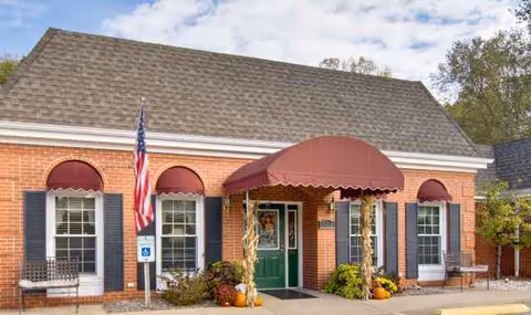 Brick senior living facility exterior with green door, maroon awning, flag, and fall decor.