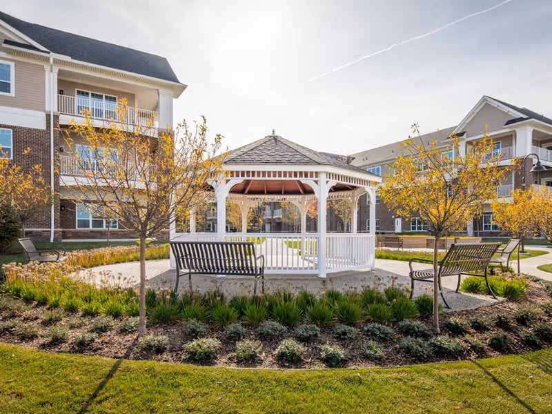 White gazebo with benches and landscaped garden in the courtyard of a senior living apartment complex.