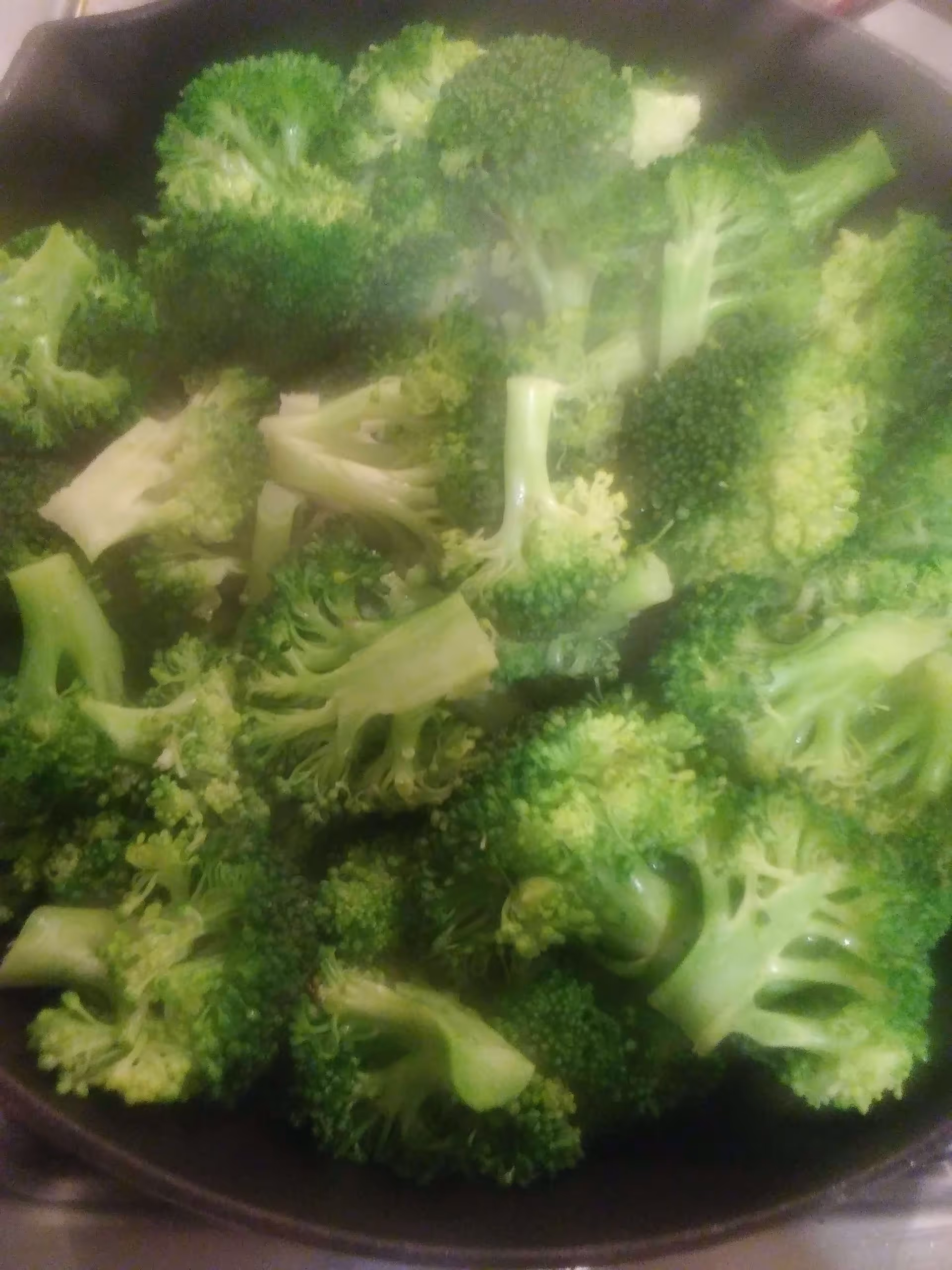 Close-up view of fresh broccoli florets in a pan, likely being cooked or prepared.