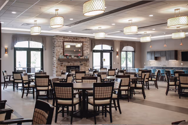 Spacious dining room with multiple round tables and chairs, a stone fireplace, pendant lights, and a service counter in the back.
