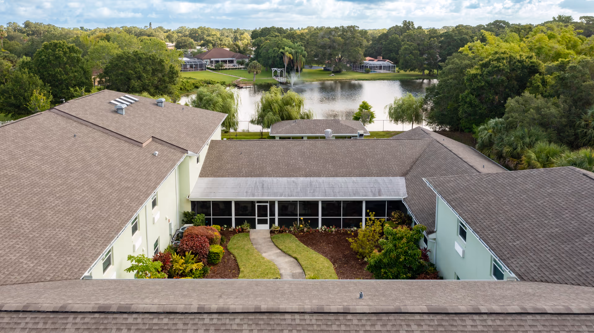 Aerial view of a U-shaped senior living building with a central courtyard, landscaping and a lake with a fountain in the background.