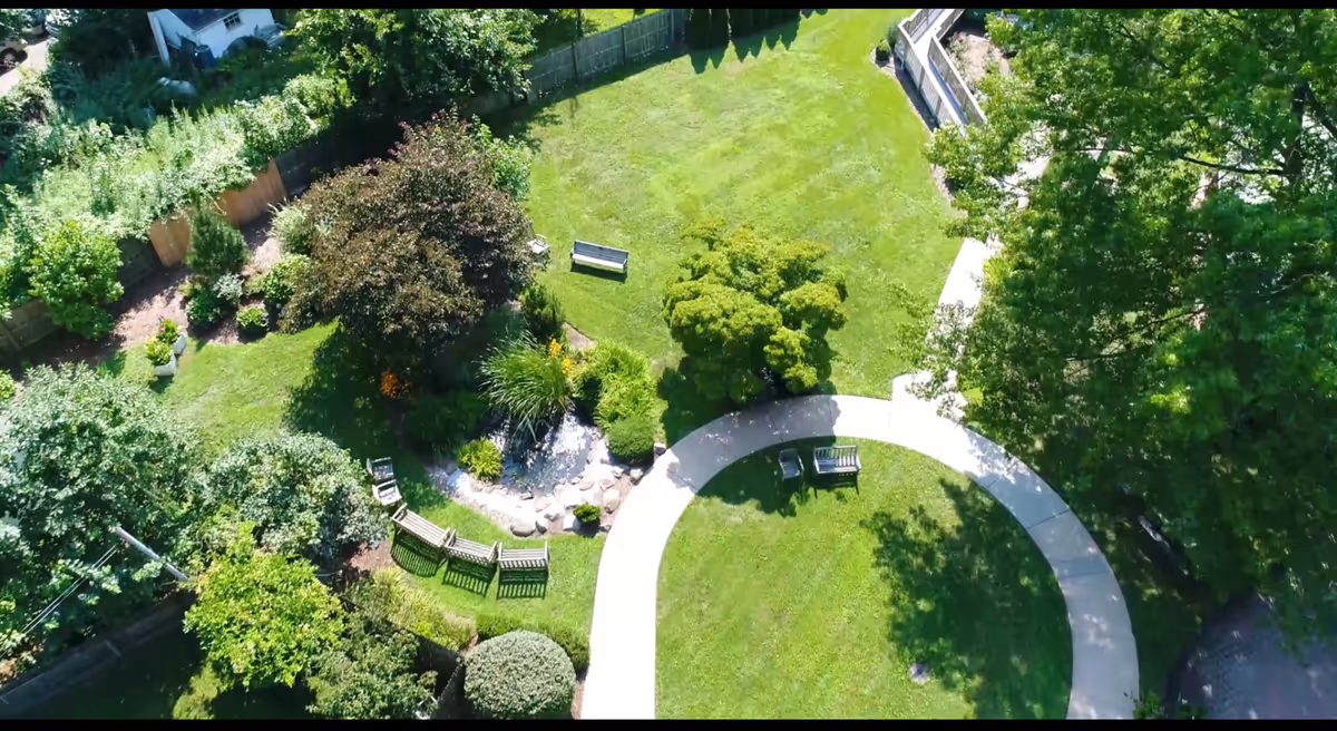 Aerial view of a landscaped circular courtyard with a walking path, benches, trees, and a small pond.