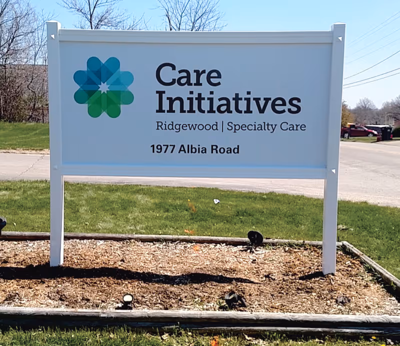 Outdoor sign for Care Initiatives Ridgewood Specialty Care located at 1977 Albia Road, with a green and blue geometric logo on the left side of the sign.