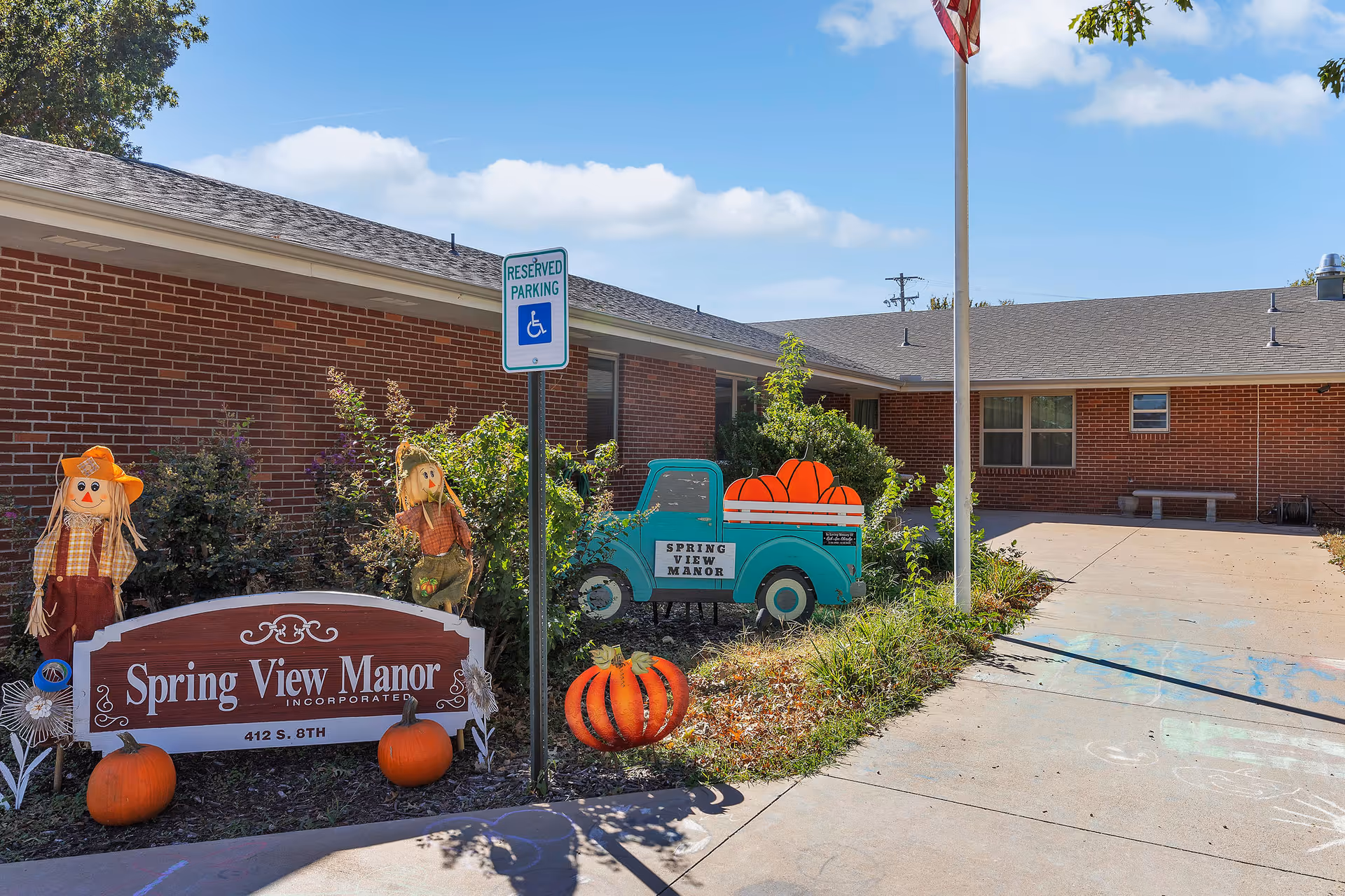 Front entrance of Spring View Manor's brick building with a sign, seasonal pumpkin decorations, and a reserved parking sign.