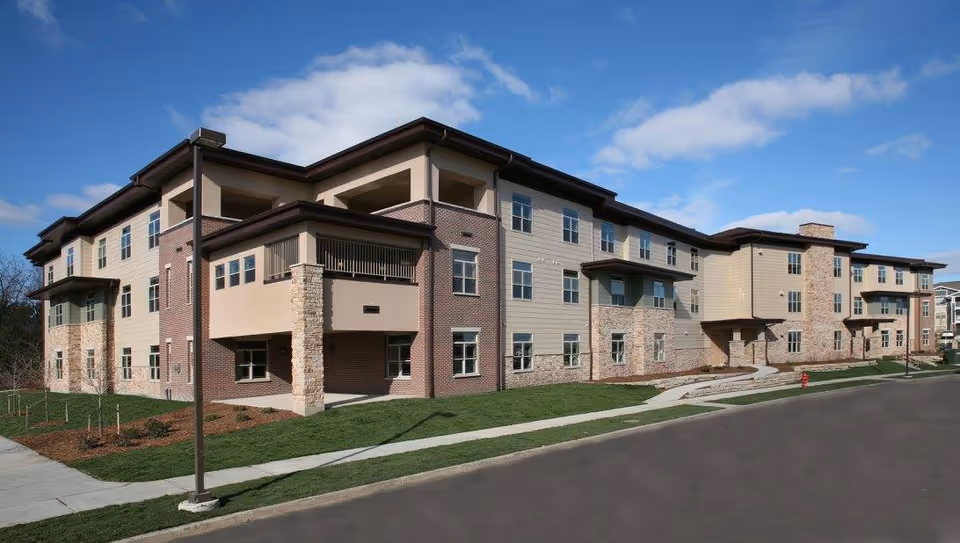 A modern, multi-story senior living facility with brick and beige siding along a street.