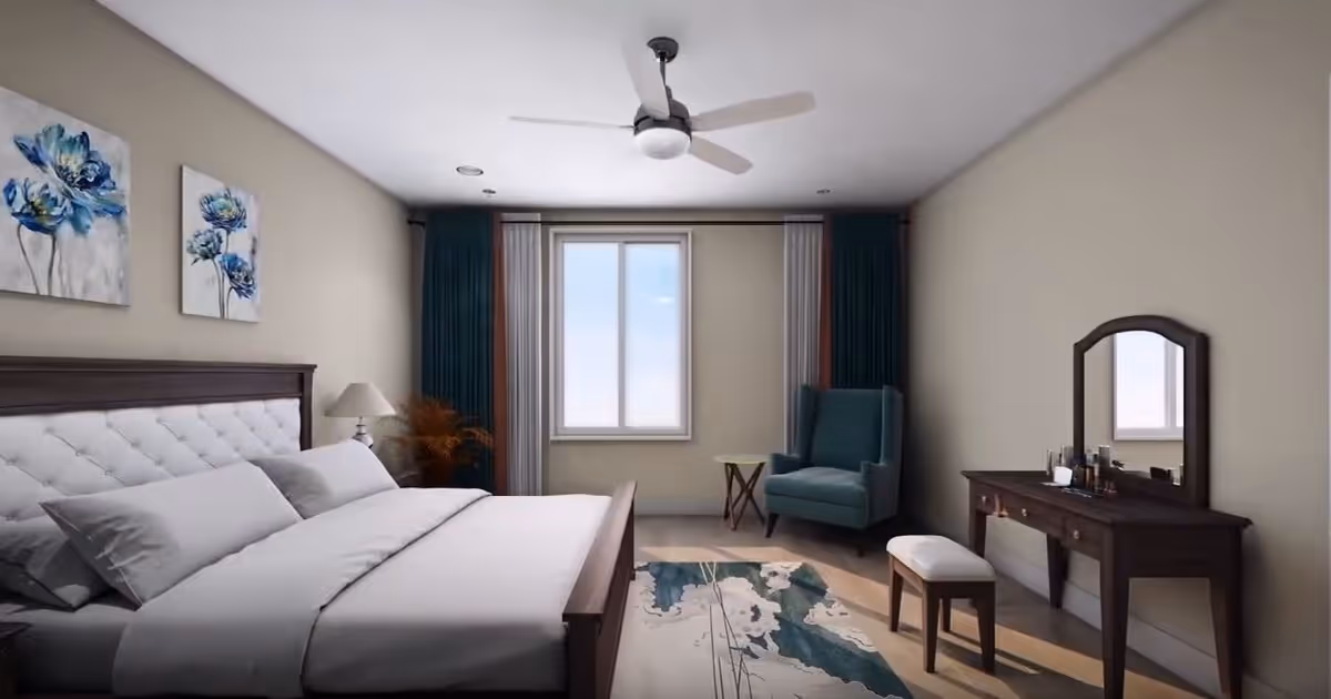 A neatly arranged bedroom with a large bed featuring white bedding and pillows, a wooden headboard, two blue floral paintings on the wall above the bed, a bedside lamp on a small table, a blue armchair next to a window with curtains, a wooden vanity table with a mirror and a cushioned stool, and a ceiling fan above.