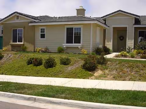 Front view of a single-story senior living facility with manicured shrubs and sidewalk.