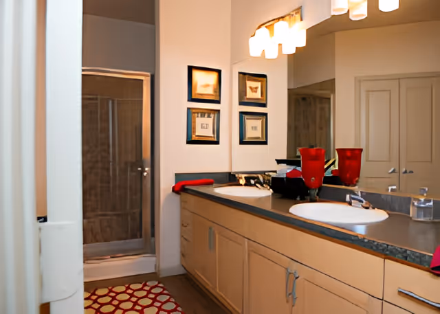 Double-sink bathroom vanity with a large mirror, decorative lights, and a glass-enclosed shower.