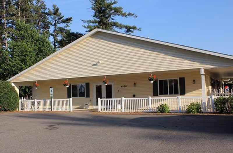 Single-story beige senior living building with white railing and hanging flower baskets.